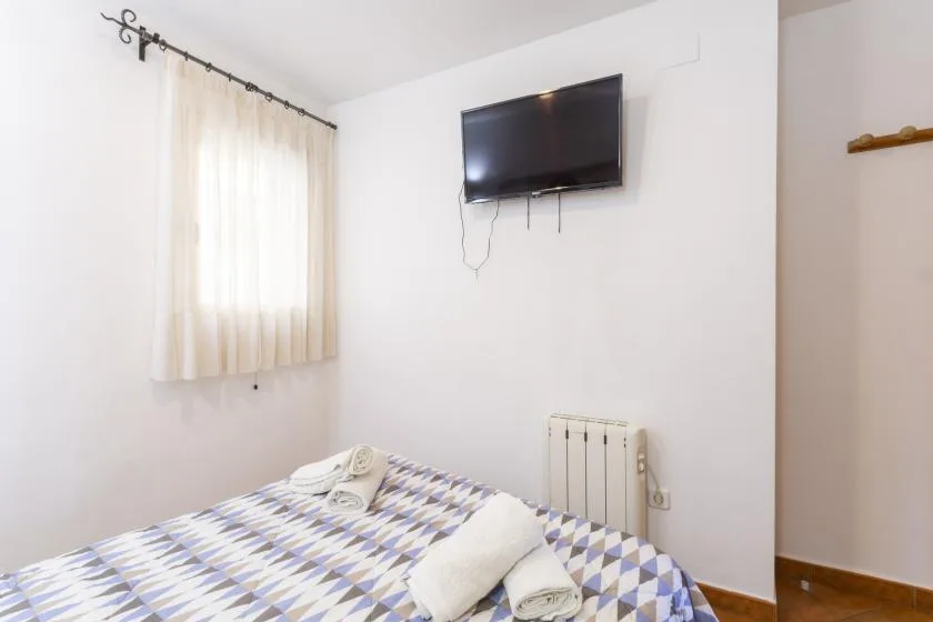 A bedroom with a patterned bed, curtained window, and wall-mounted television.