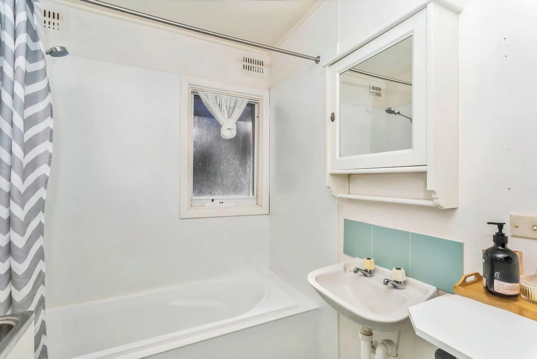 A bathroom with a bathtub, sink, and mirrored wall cabinet.