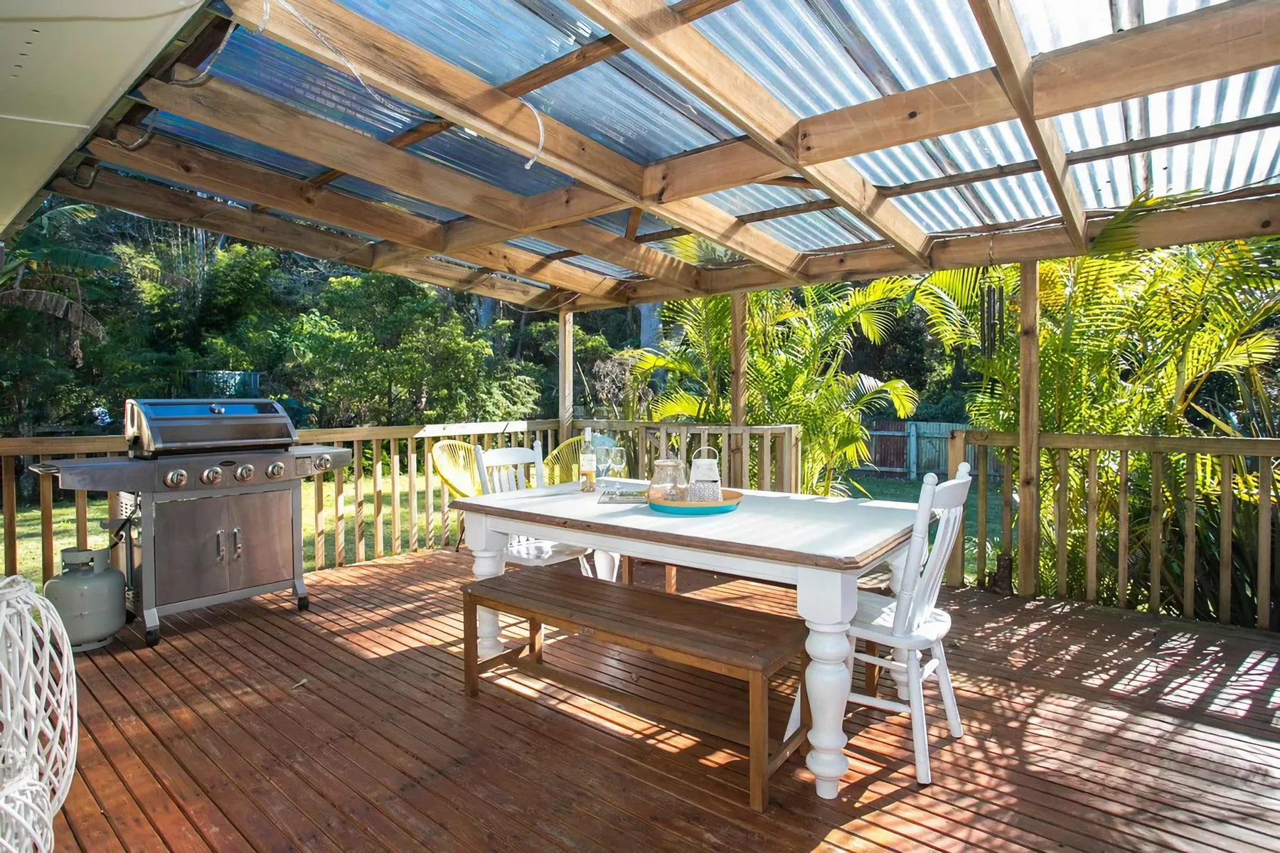 A covered outdoor dining deck with a table, seating, and a barbecue.