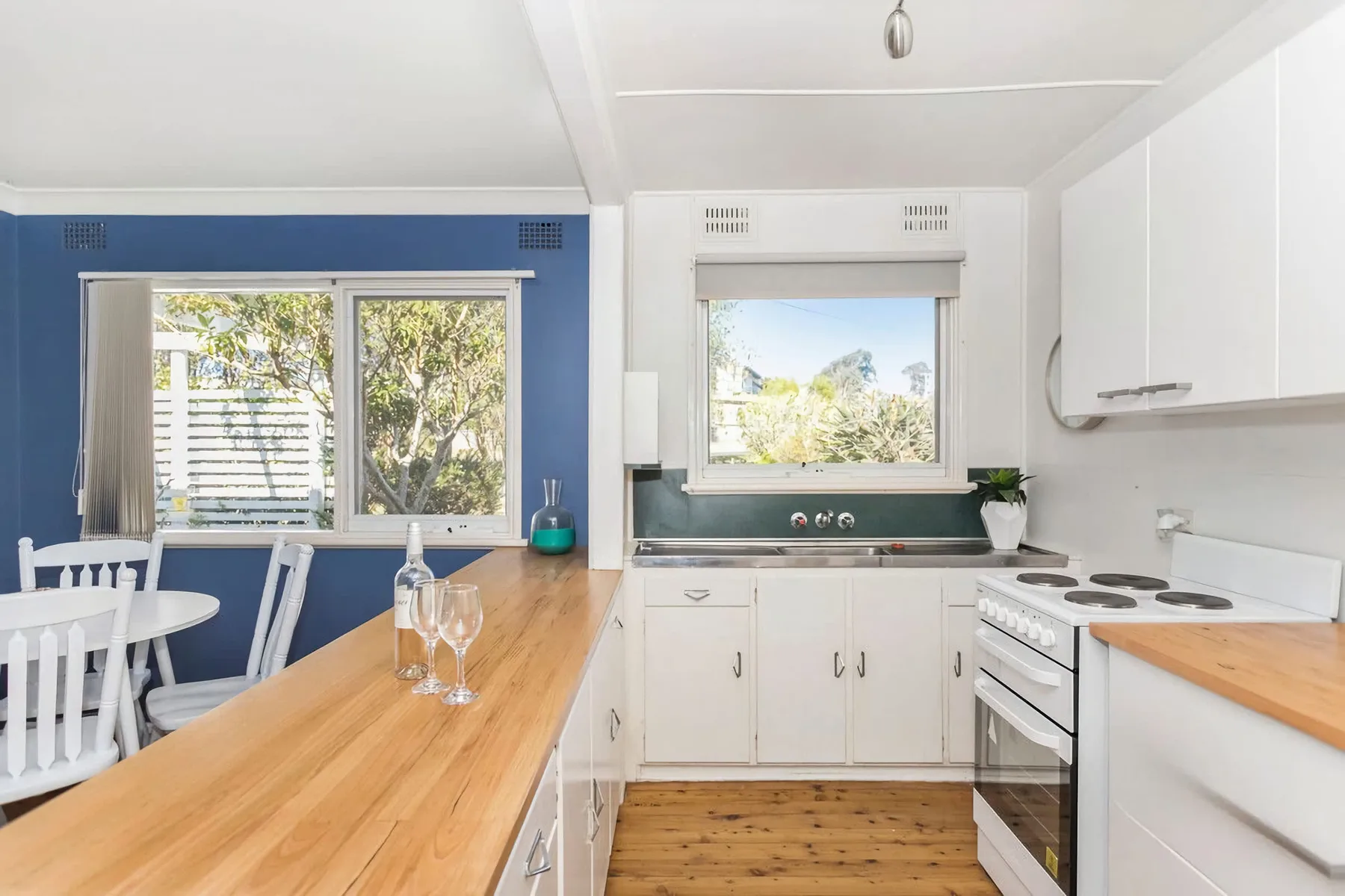 A bright kitchen with a wooden countertop, white cabinetry, and a window.