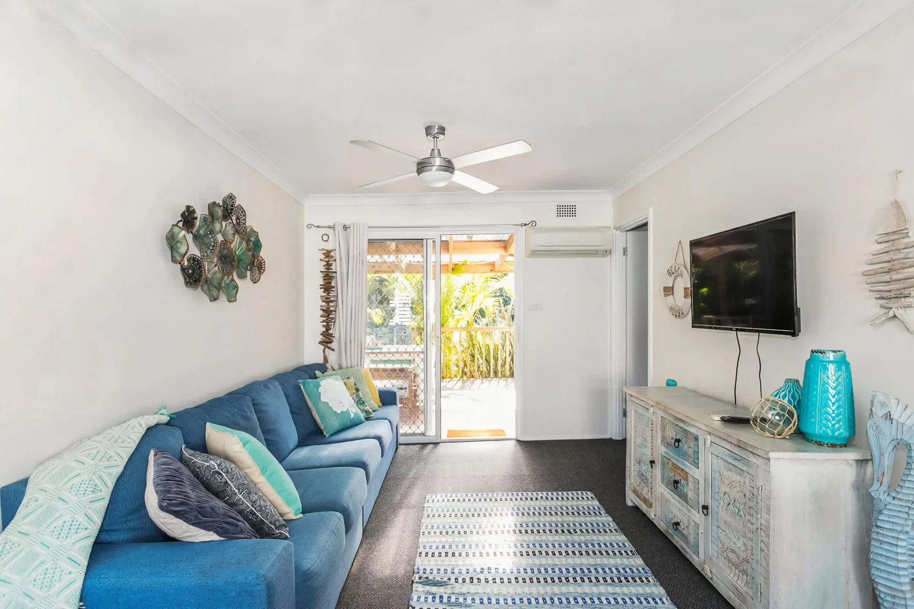 A bright living room with blue seating, a television, and glass doors opening outside.