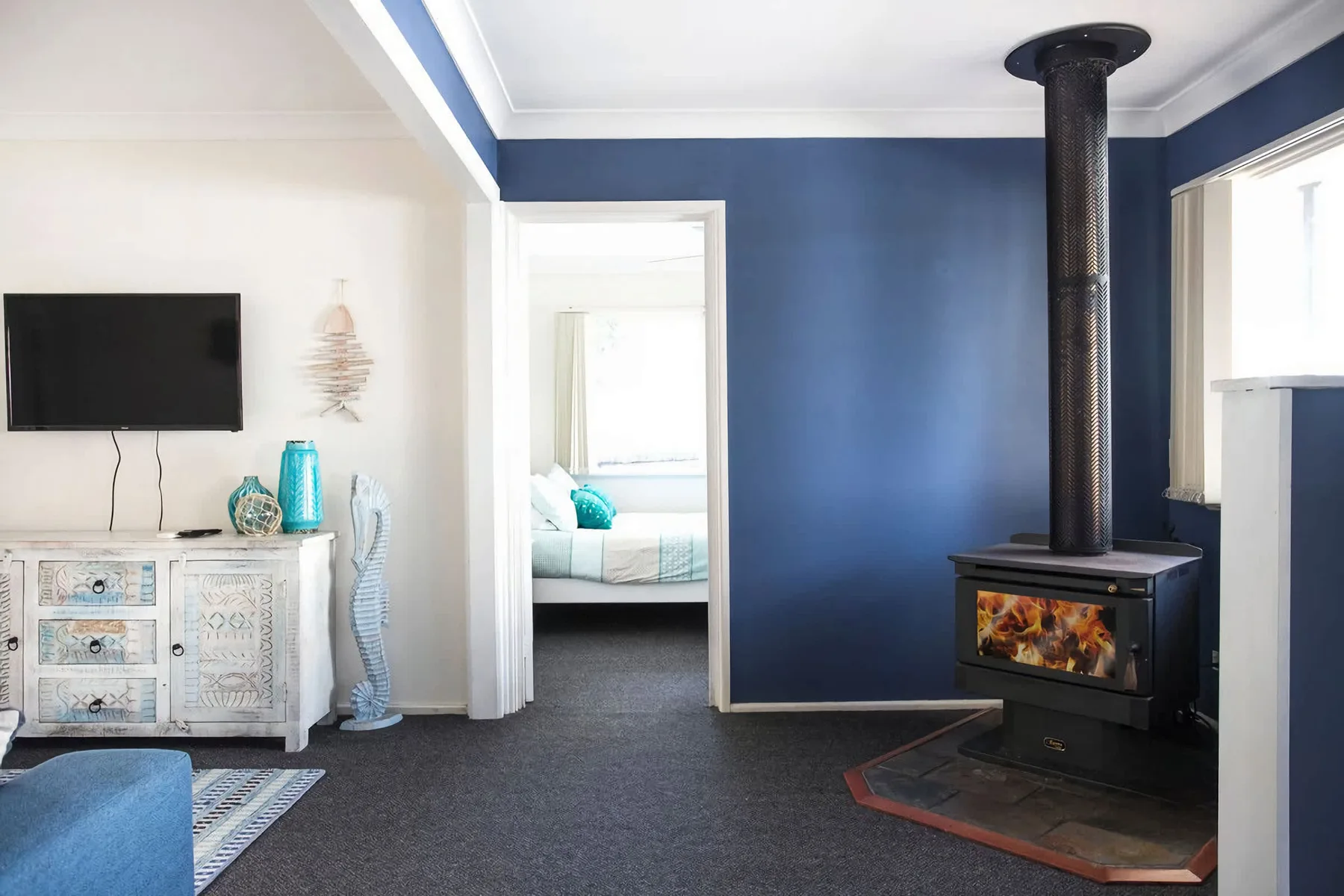 A living room with a television, blue accent wall, and wood-burning stove.