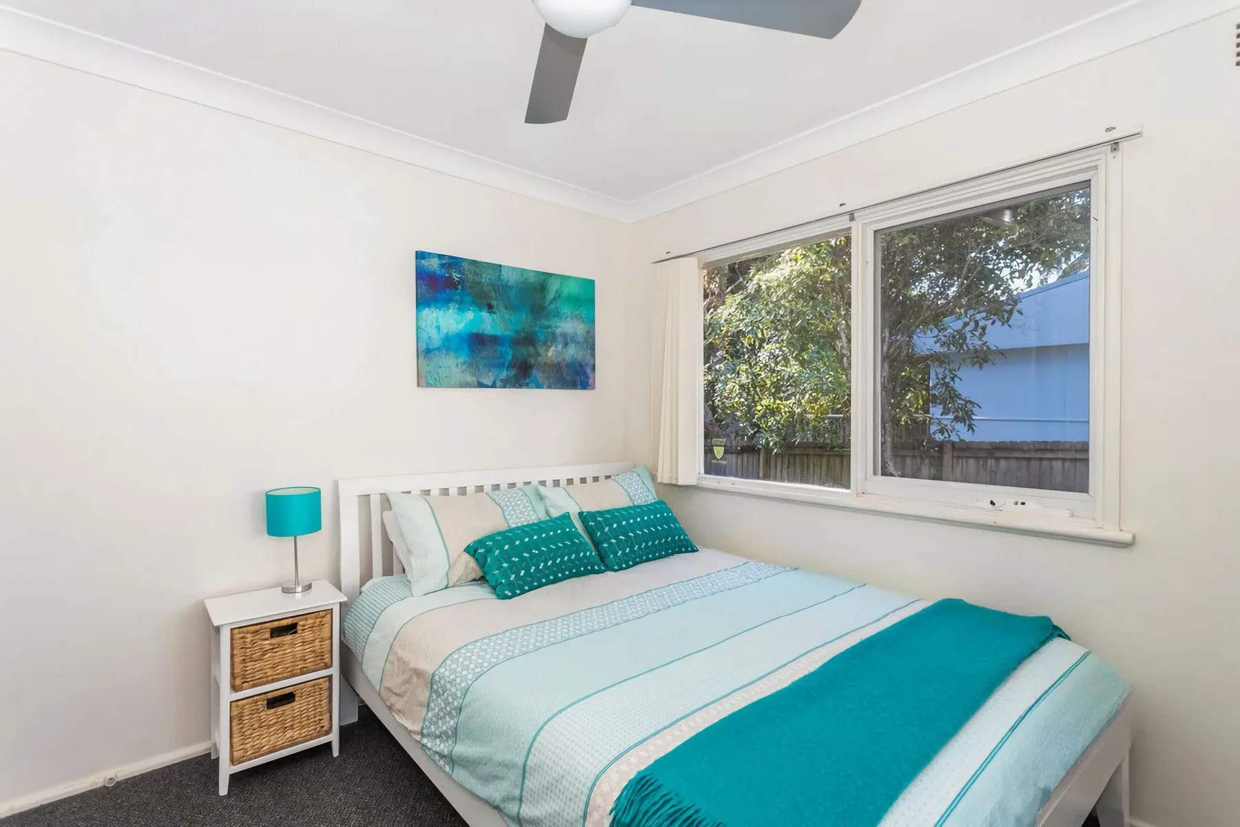 A bedroom with a neatly made bed beside large windows.