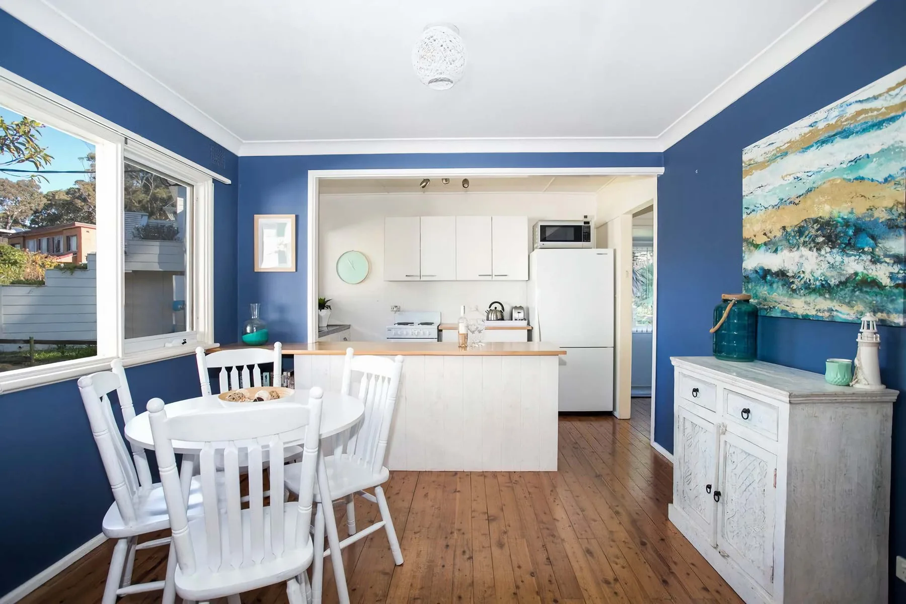 A dining area opens onto a compact kitchen, with blue walls and a wooden floor.