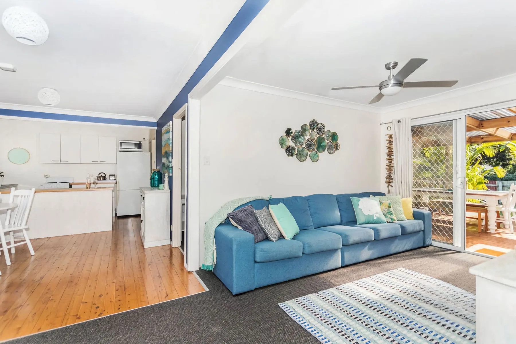A bright living room with blue seating beside an open kitchen and patio doors.
