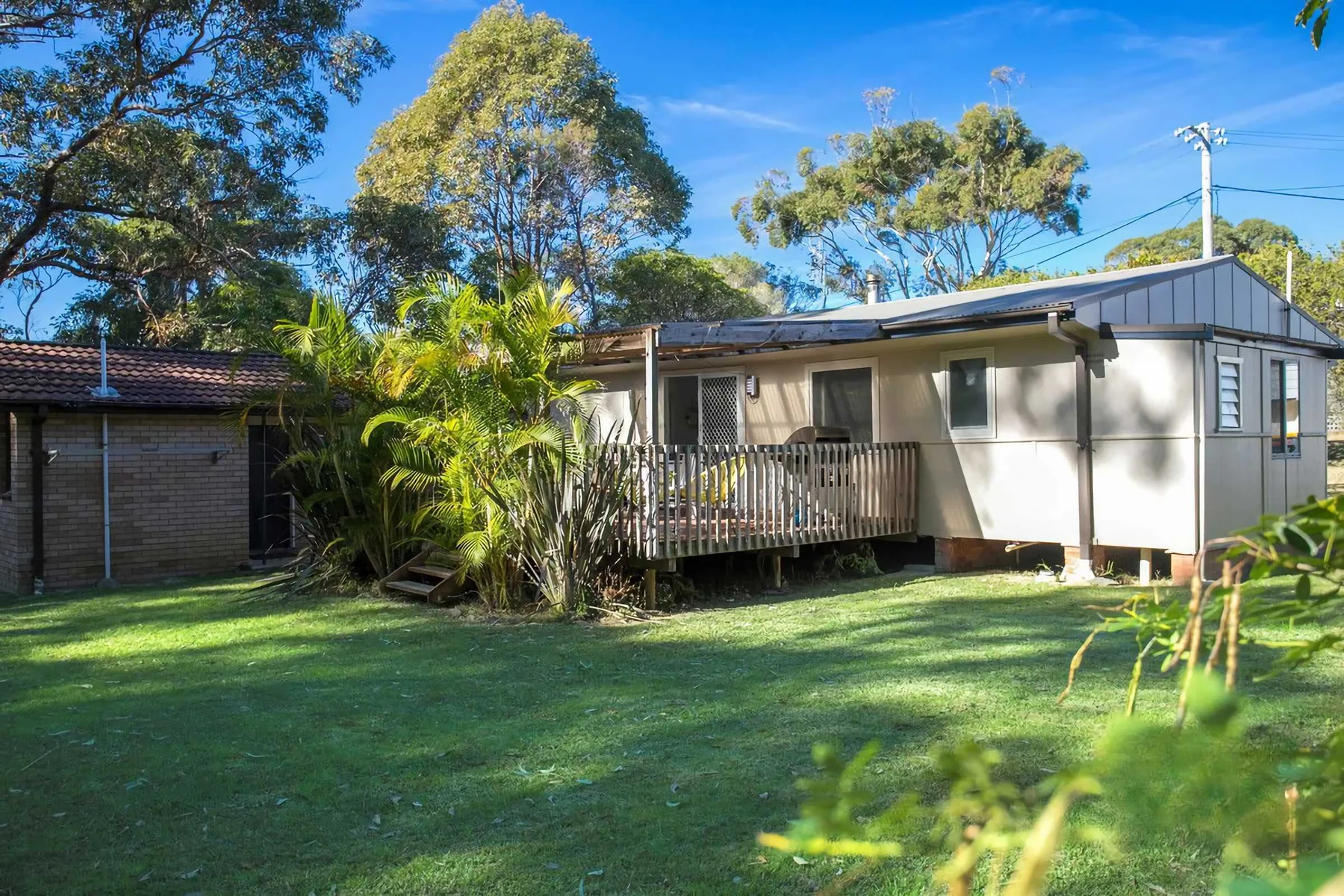 A single-story house with a small raised deck sits beside a green lawn.