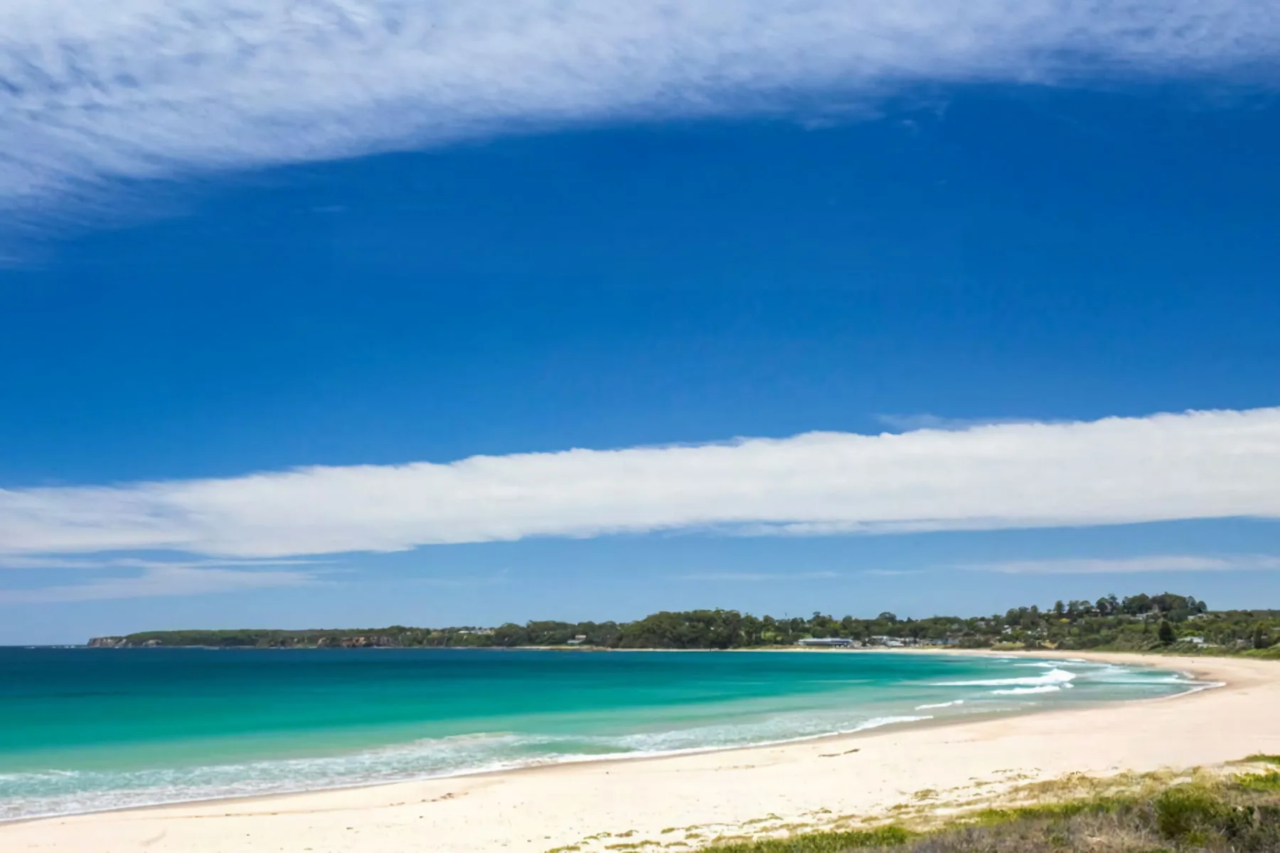 A sandy beach curves alongside turquoise water beneath a blue sky.