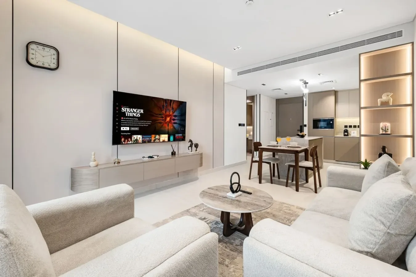 Una sala de estar moderna se abre a un comedor, con un televisor montado en la pared.