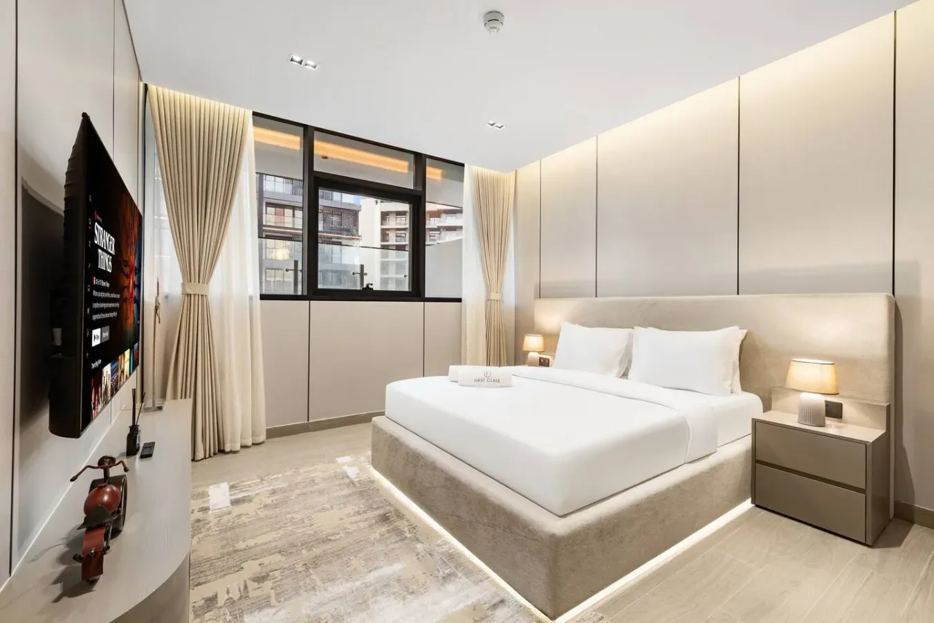 Un dormitorio con una cama tendida, mesitas de noche y un televisor en la pared.