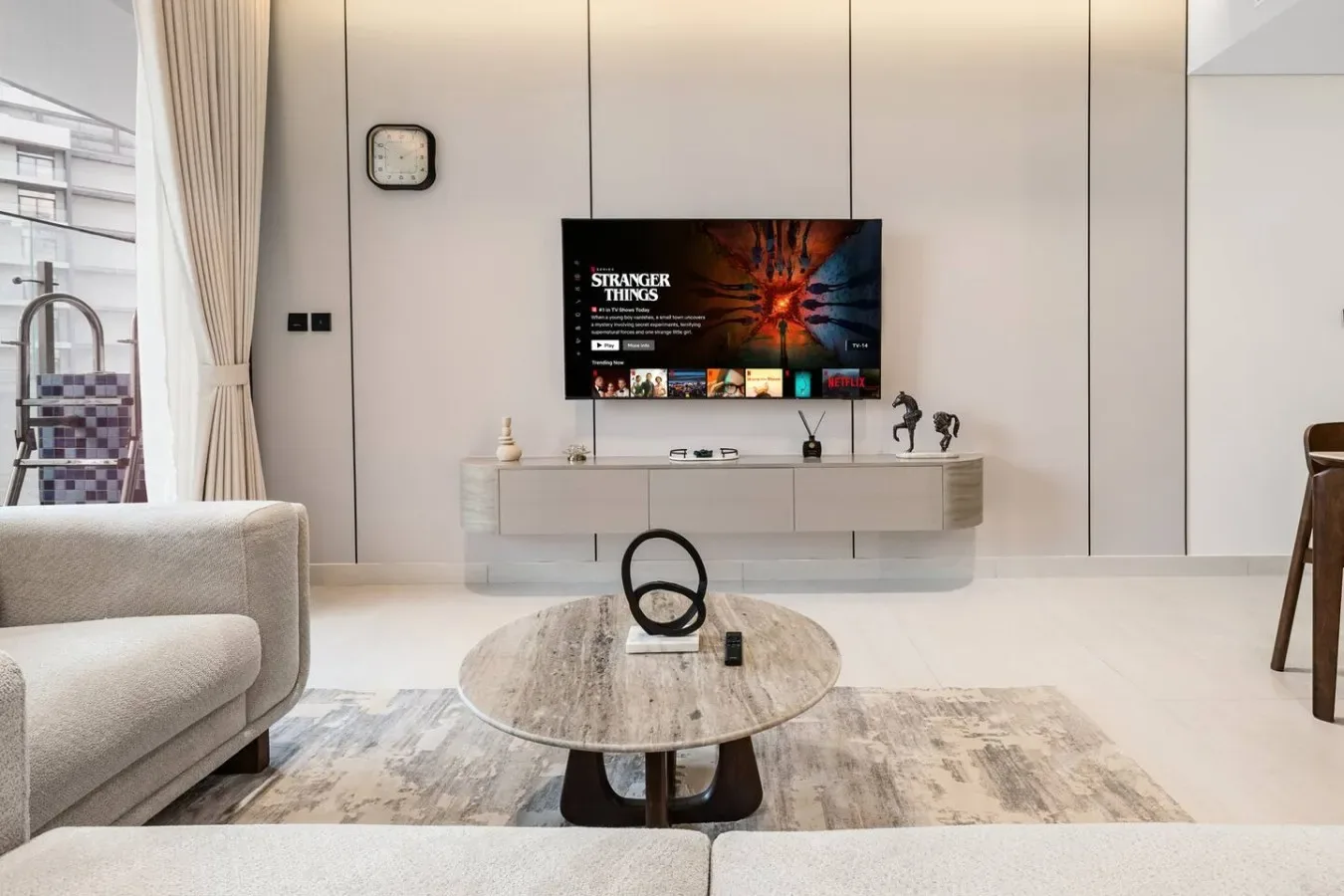 Una sala luminosa con un televisor montado en la pared sobre un mueble bajo.