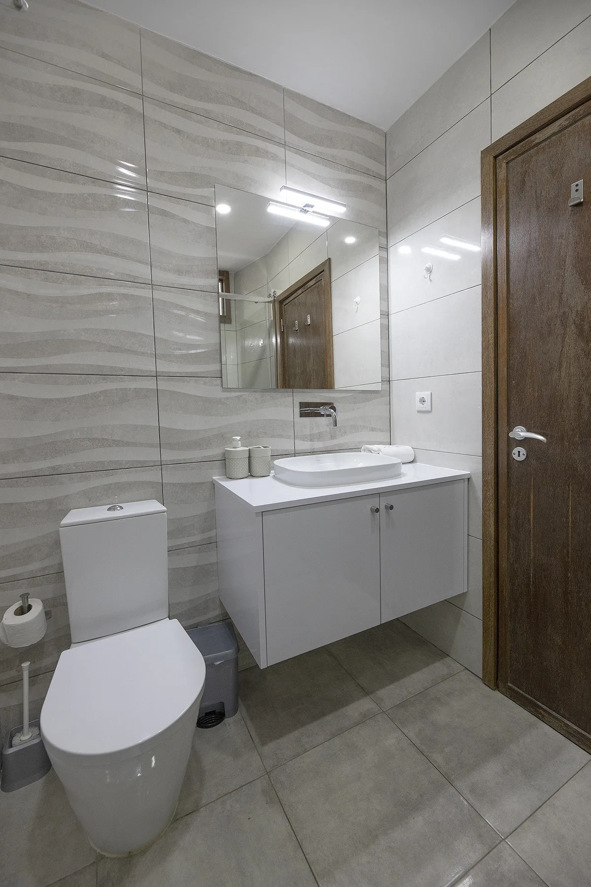 A tiled bathroom with a toilet, sink, and mirrored vanity.