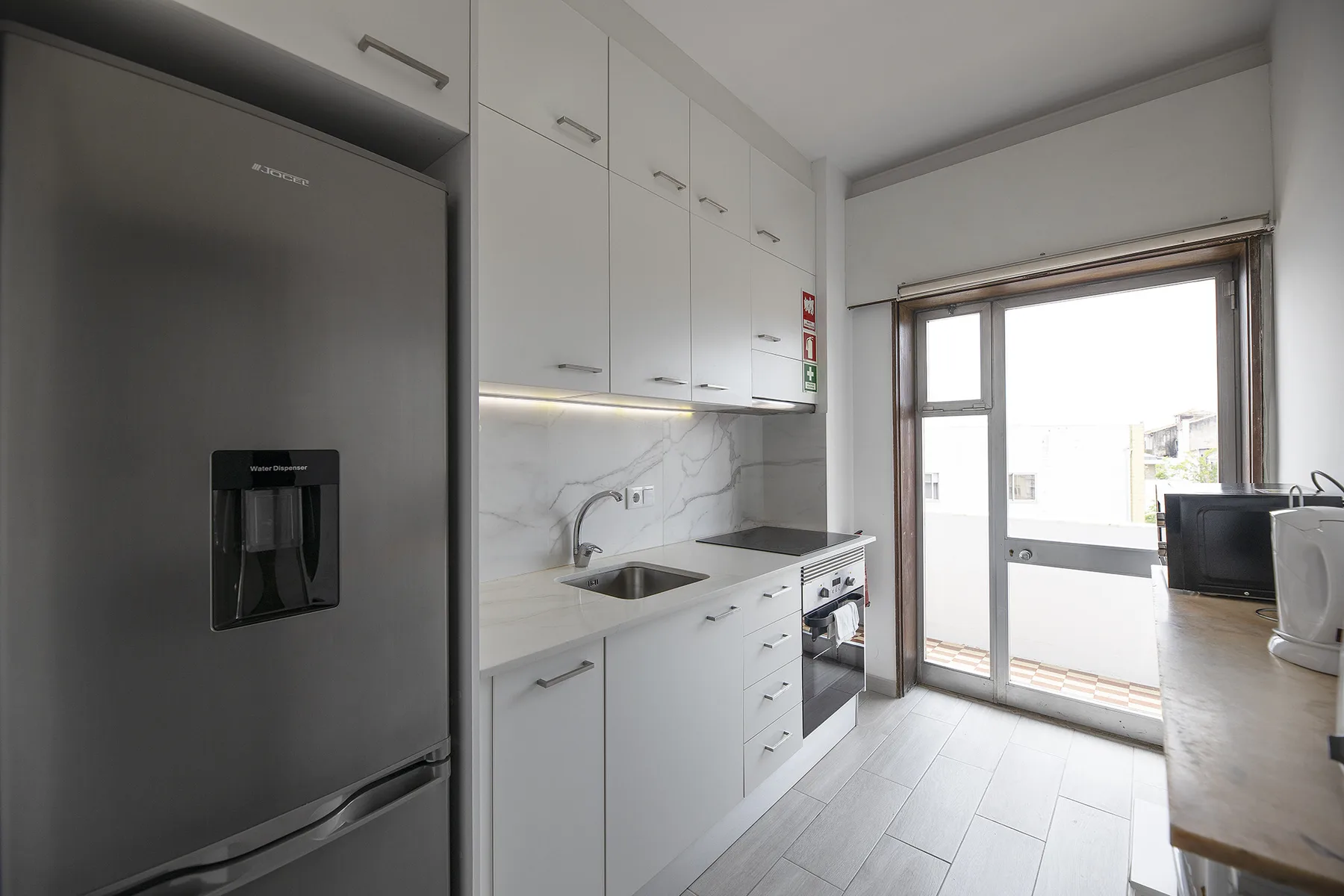 A bright kitchen with white cabinets, a sink, and a refrigerator.
