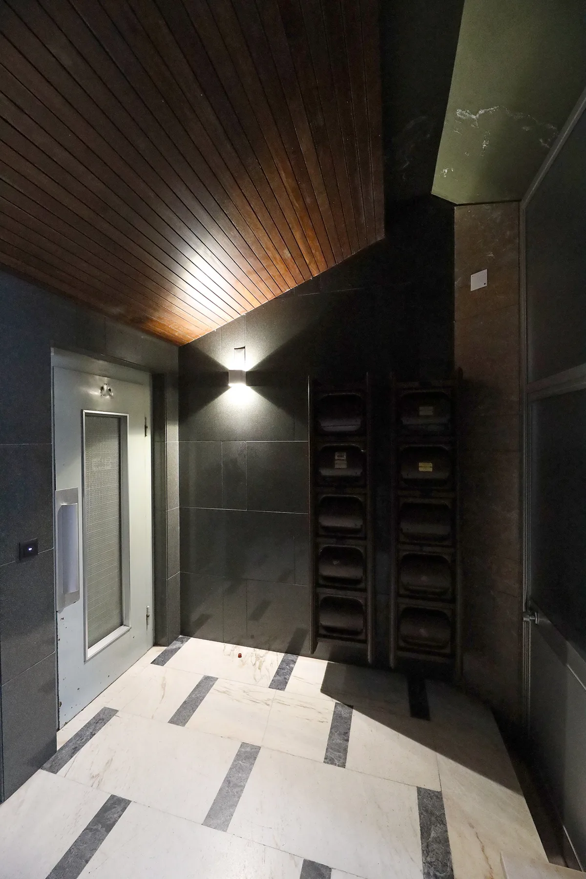 A building entrance hallway with a glass door, dark walls, and a tiled floor.