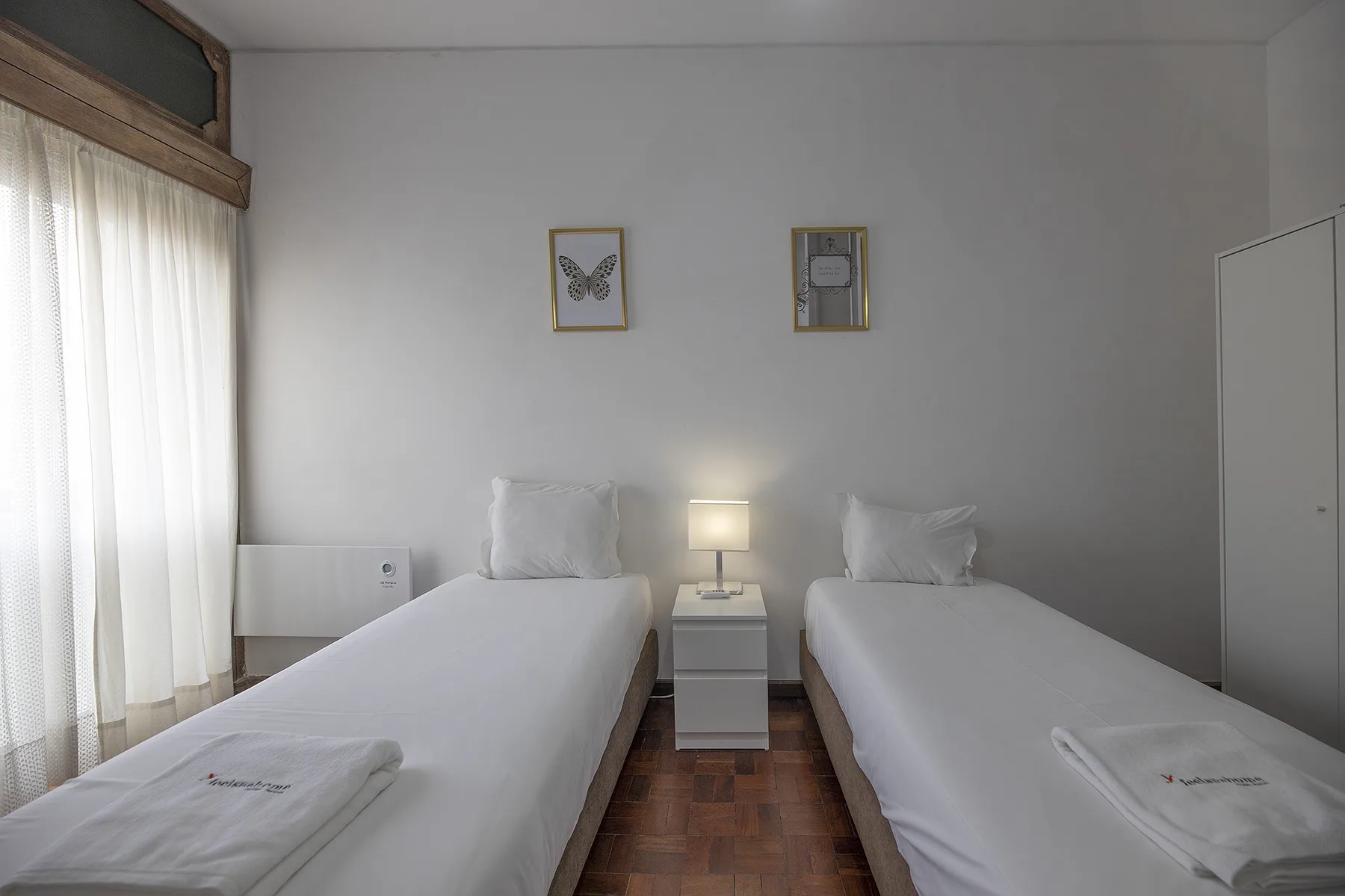 A bedroom with two single beds, a nightstand, and framed pictures on the wall.