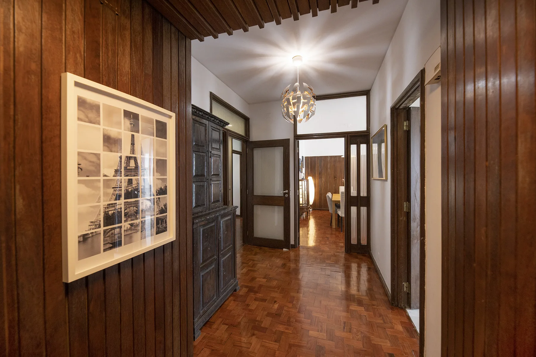 A wood-paneled hallway with framed artwork and open doorways.