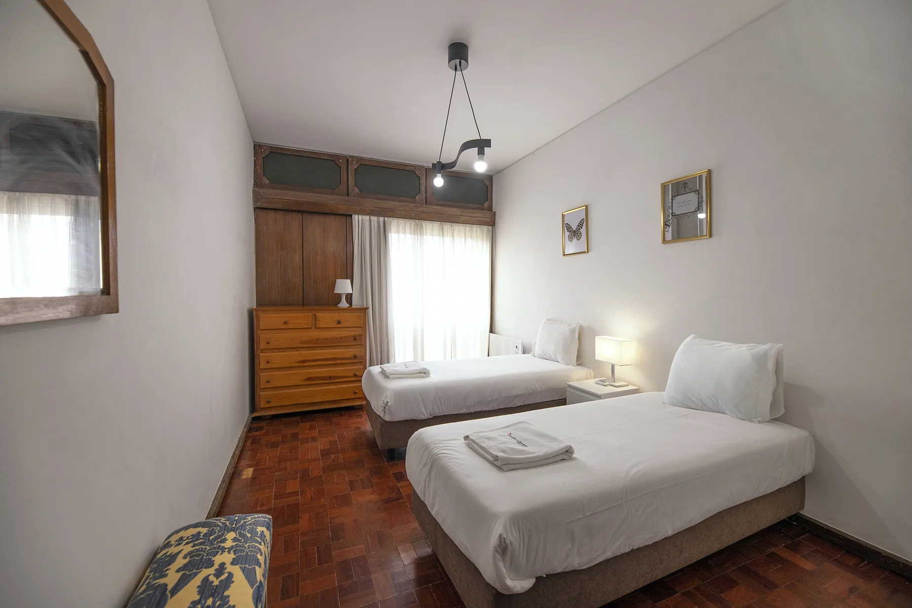 A bedroom with two beds, a wooden wardrobe, and polished wood flooring.
