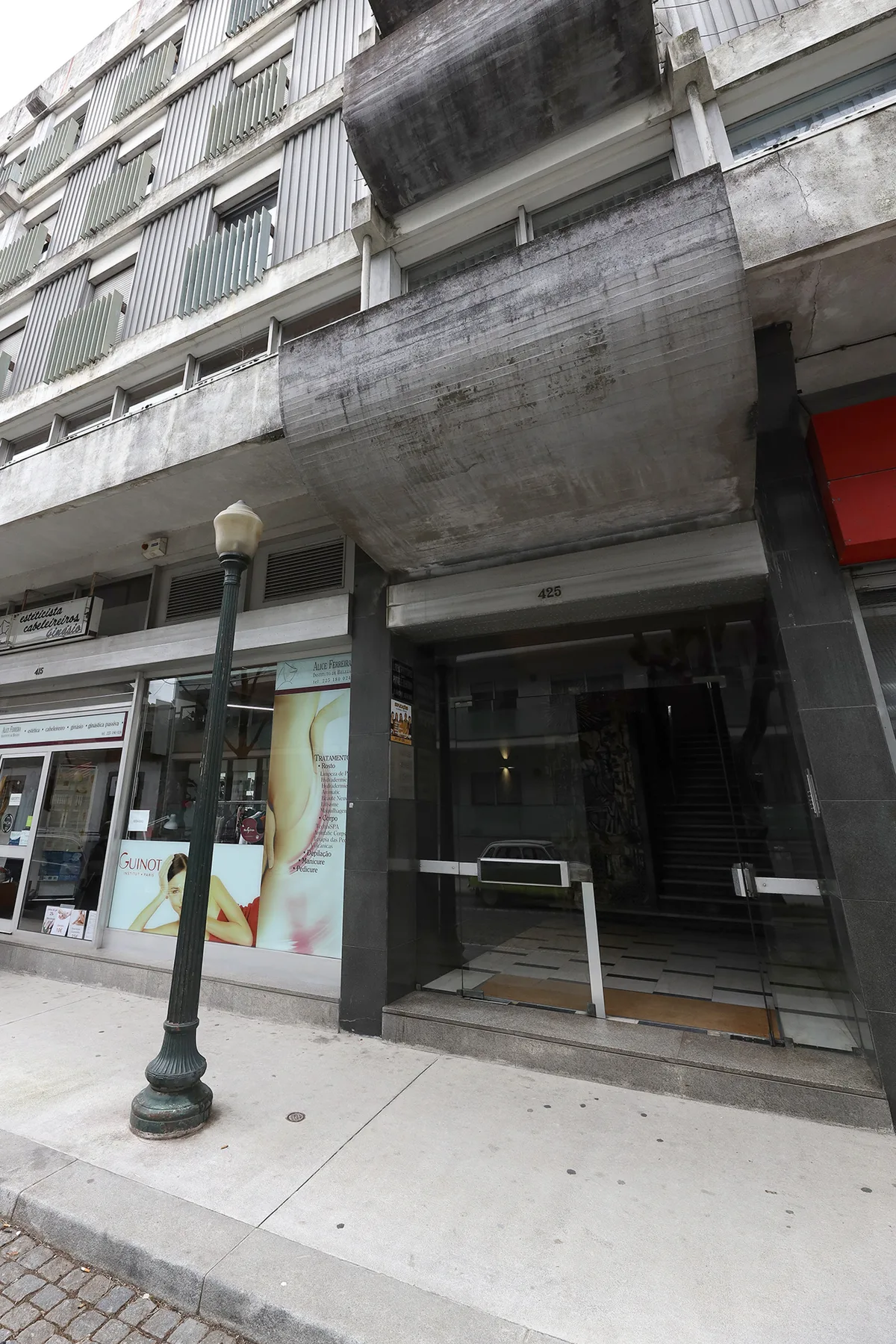 A concrete apartment building entrance faces a sidewalk with storefronts.