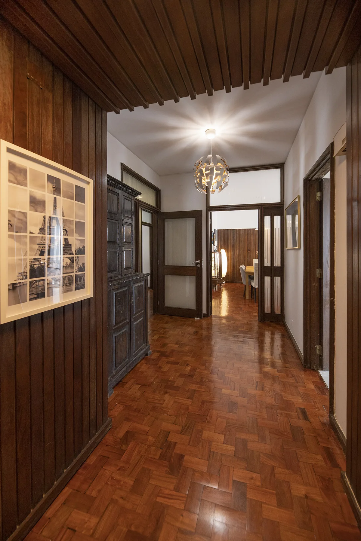 A wood-paneled hallway with a polished parquet floor and doors opening into adjoining rooms.