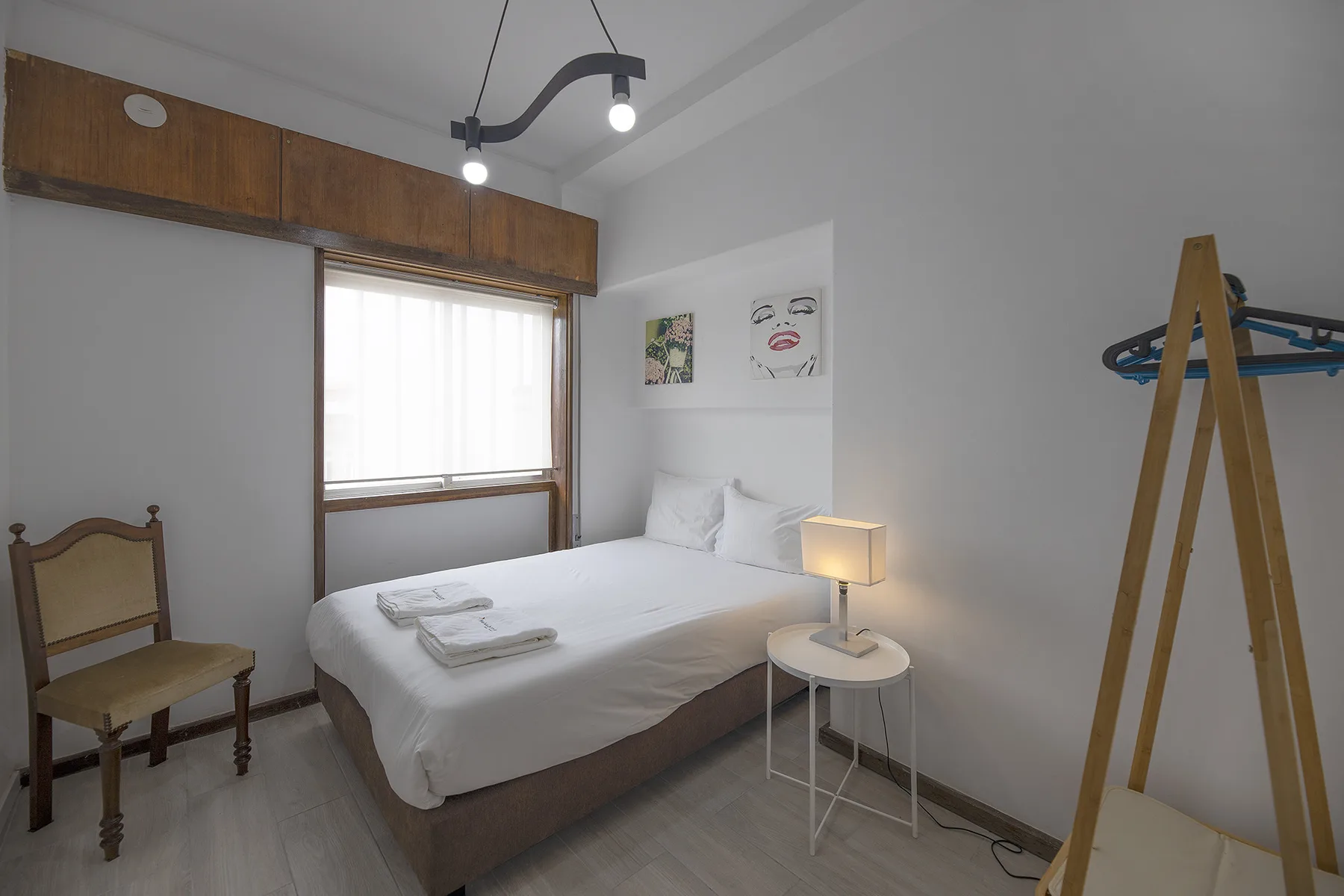 A bedroom with a neatly made bed, a small bedside table, and wall art.