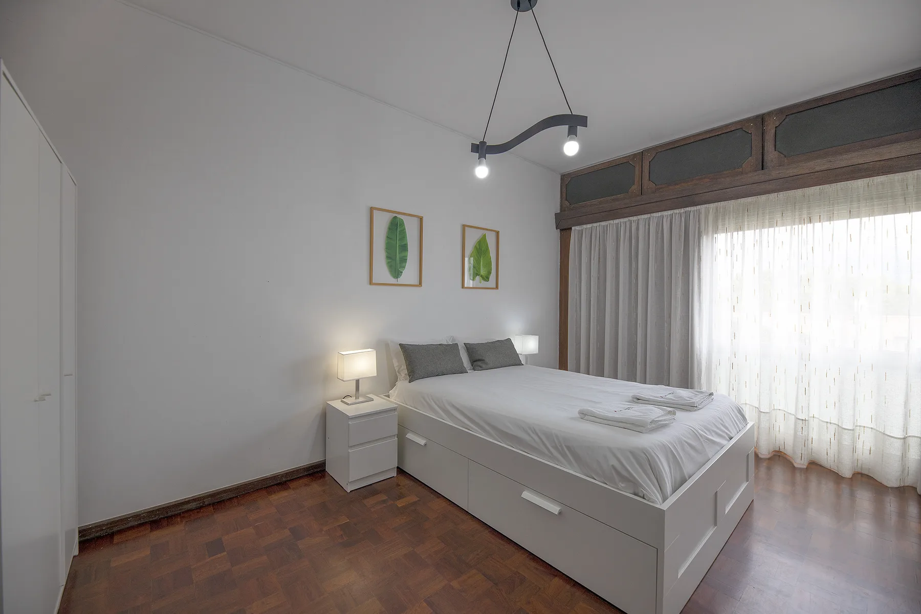 A bedroom with a bed, bedside table, and large curtained window.