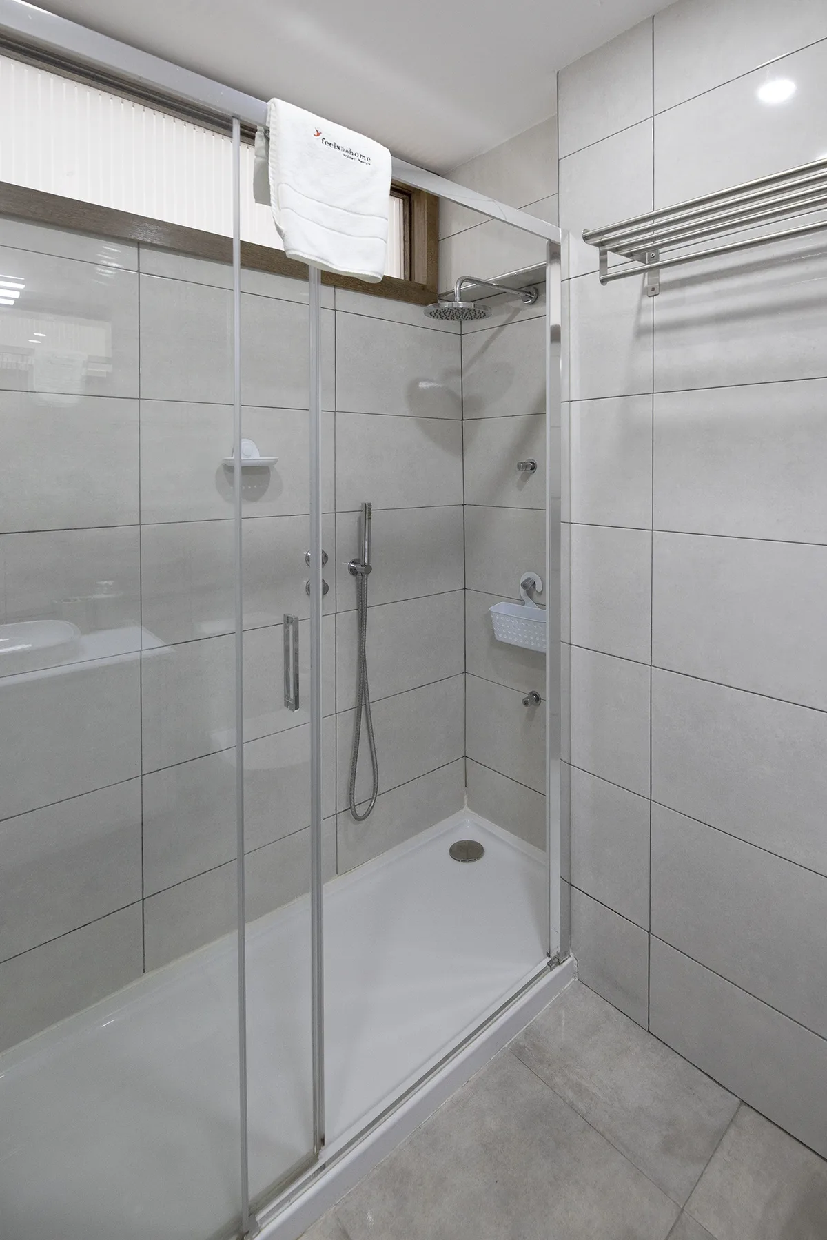 A tiled bathroom with a glass-enclosed shower and a towel hanging nearby.