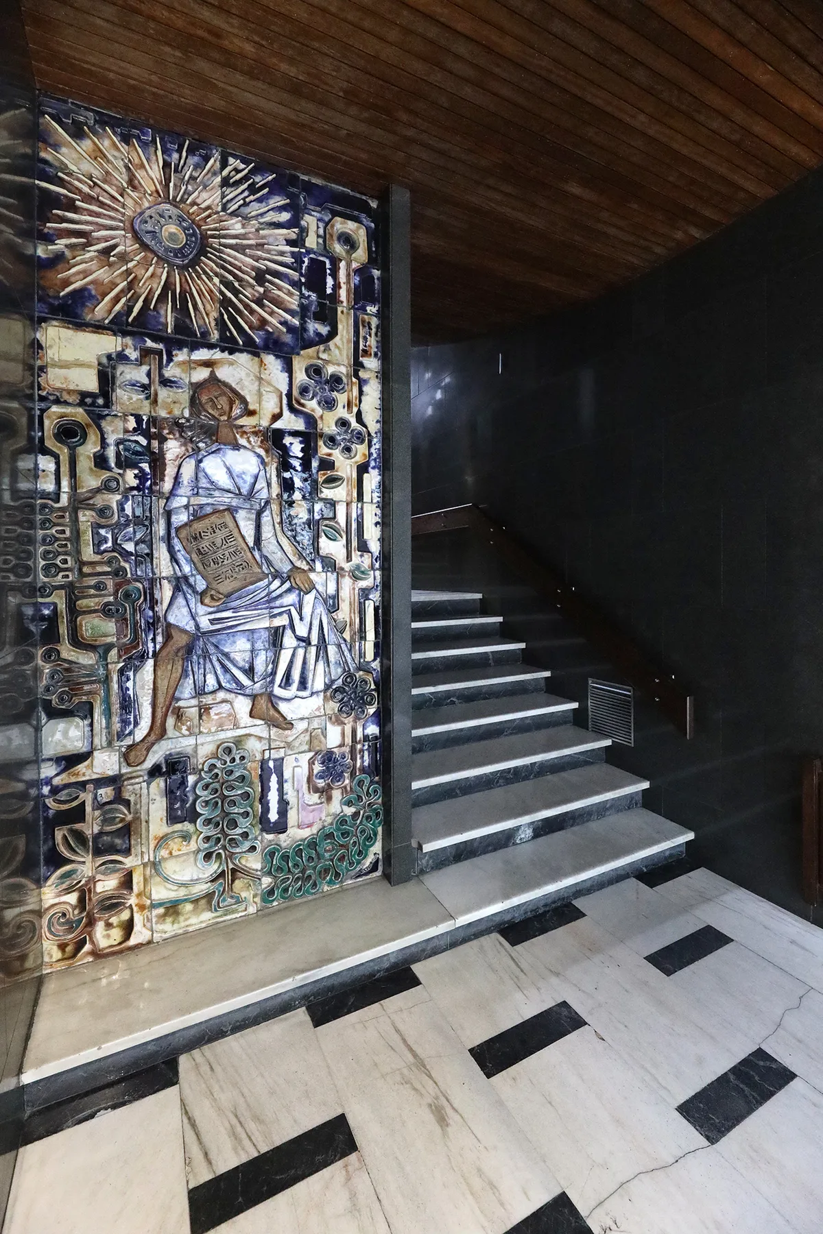 A tiled entrance hall with a staircase rising beside a decorative mosaic.