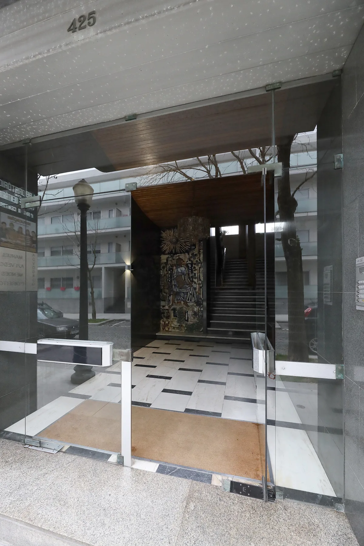 A glass entrance opens onto a tiled lobby with a staircase at the back.