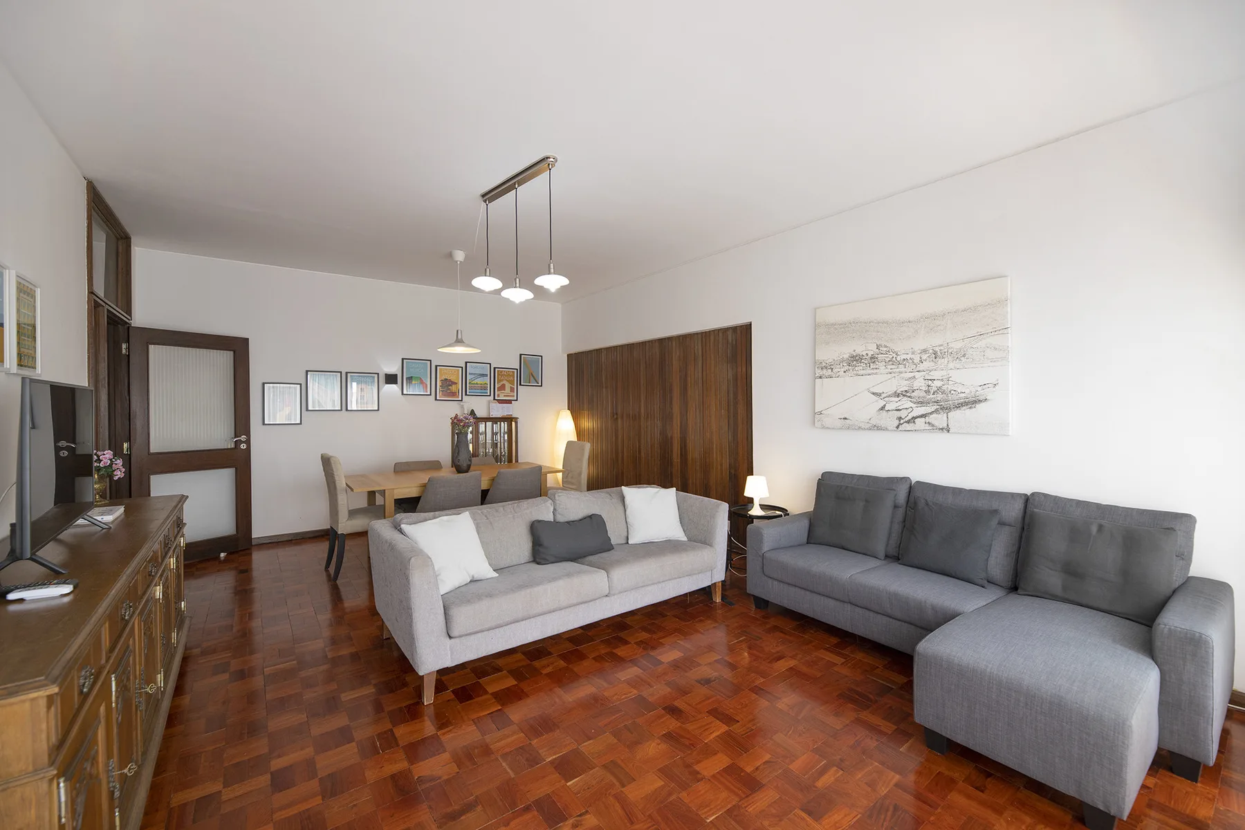 A living room with gray seating, a wooden floor, and framed artwork.