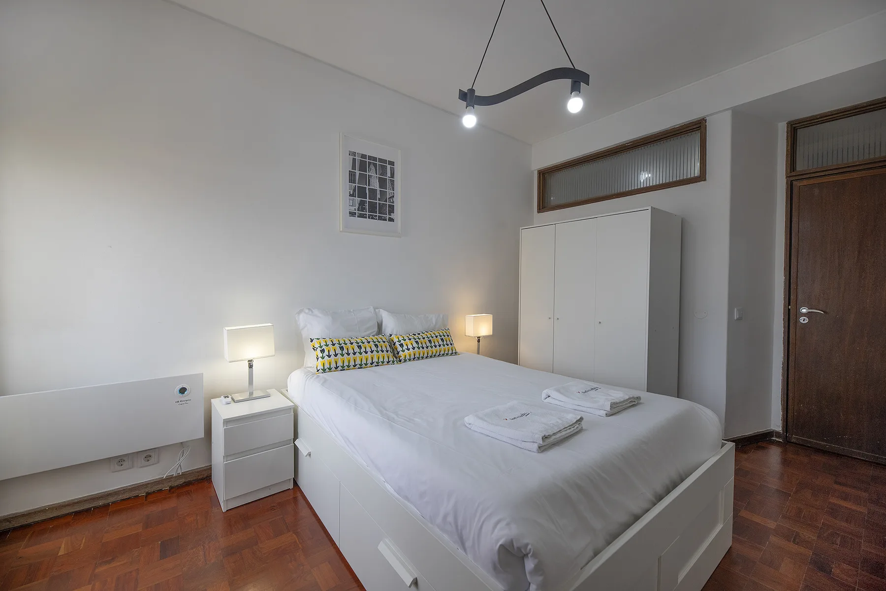 A bedroom with a neatly made bed, bedside tables, and a wardrobe.