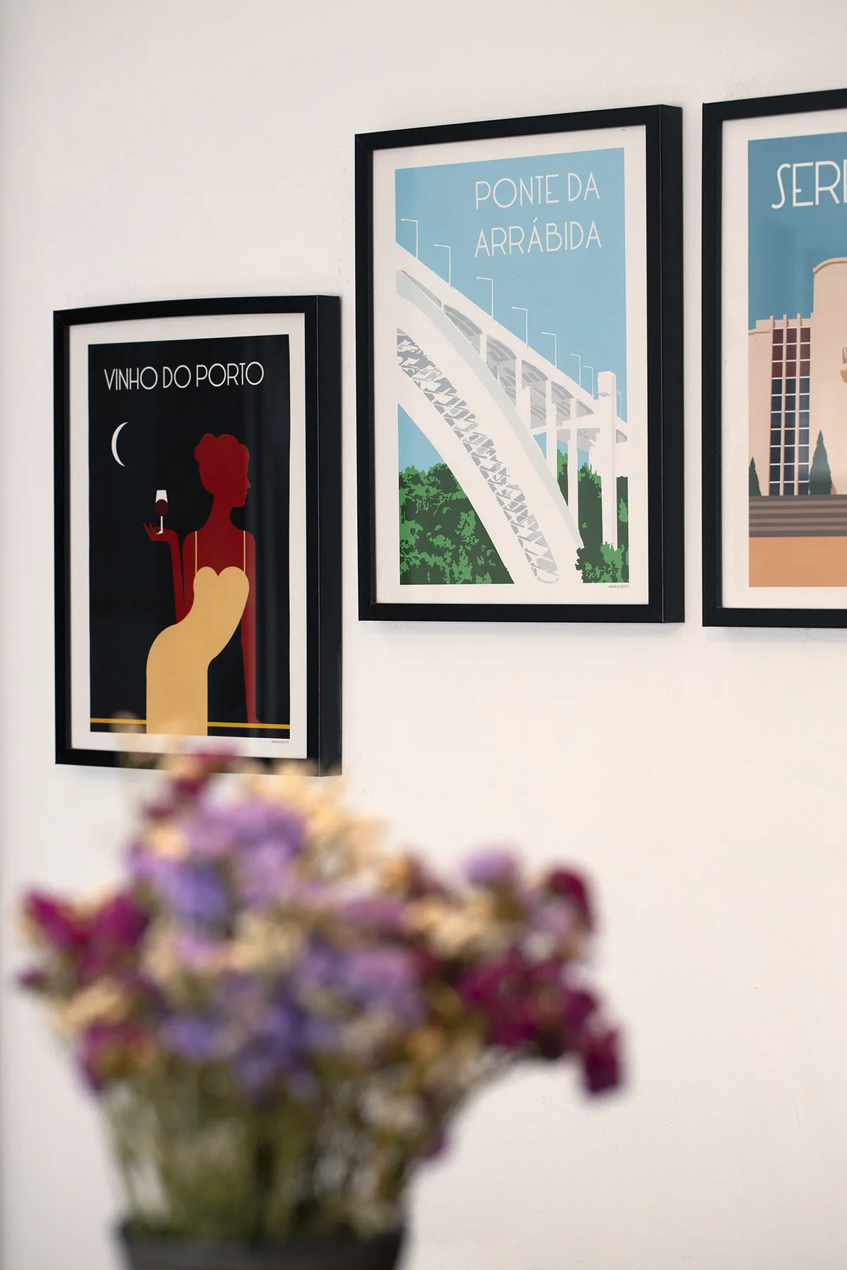 Framed prints hang on a light wall behind a vase of flowers.