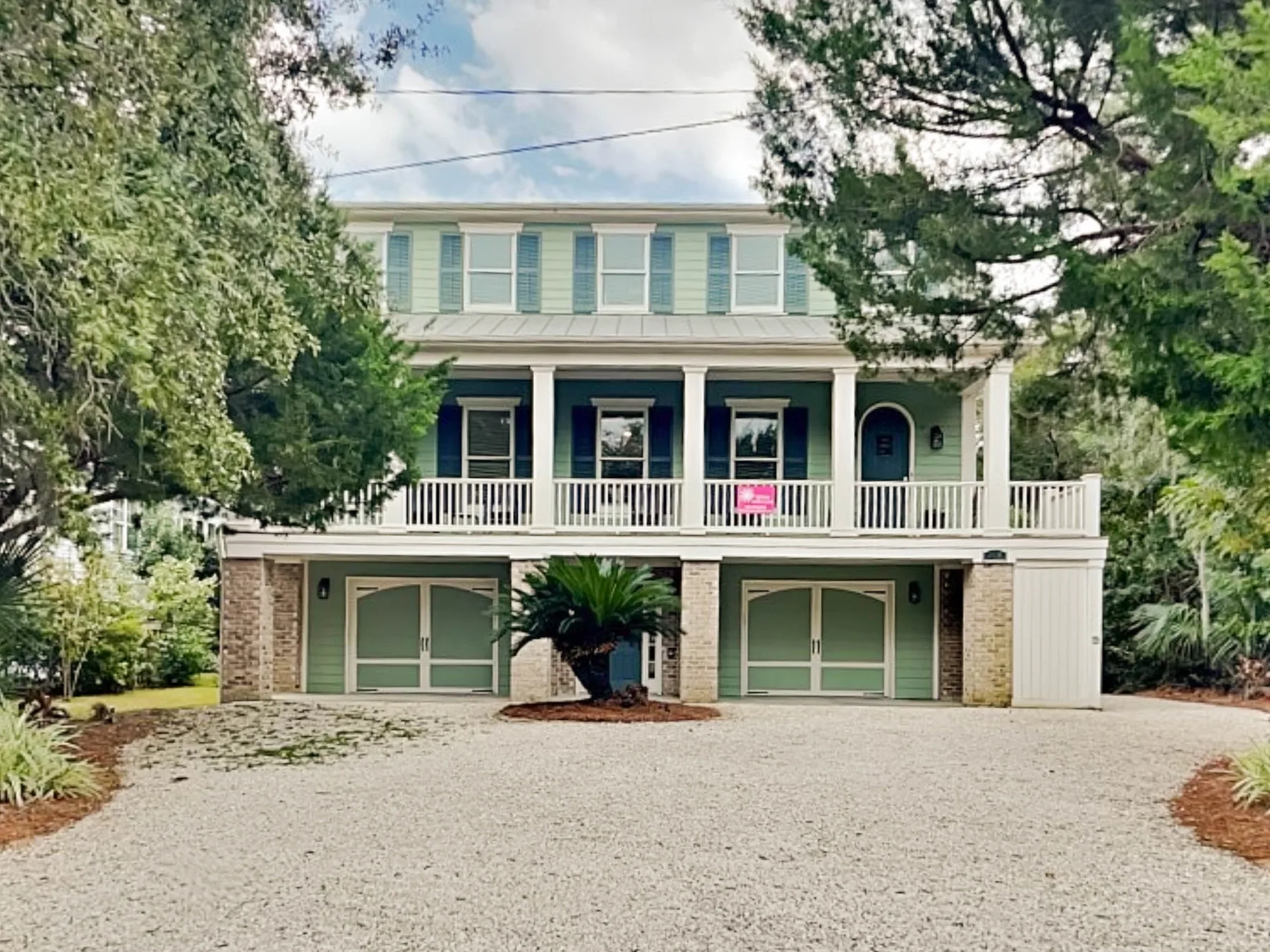 A pale green two-story house with a broad driveway and a balcony.