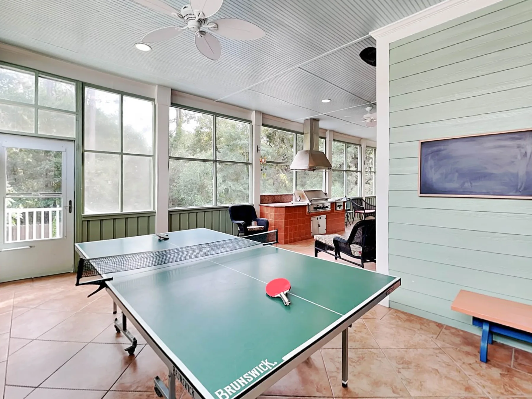 Una sala de recreación luminosa cuenta con una mesa de ping-pong verde y ventanas grandes.