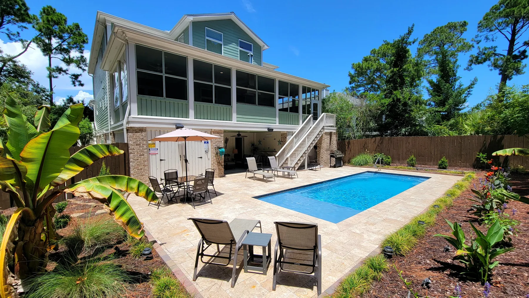 A backyard pool patio with outdoor seating beside a raised house.