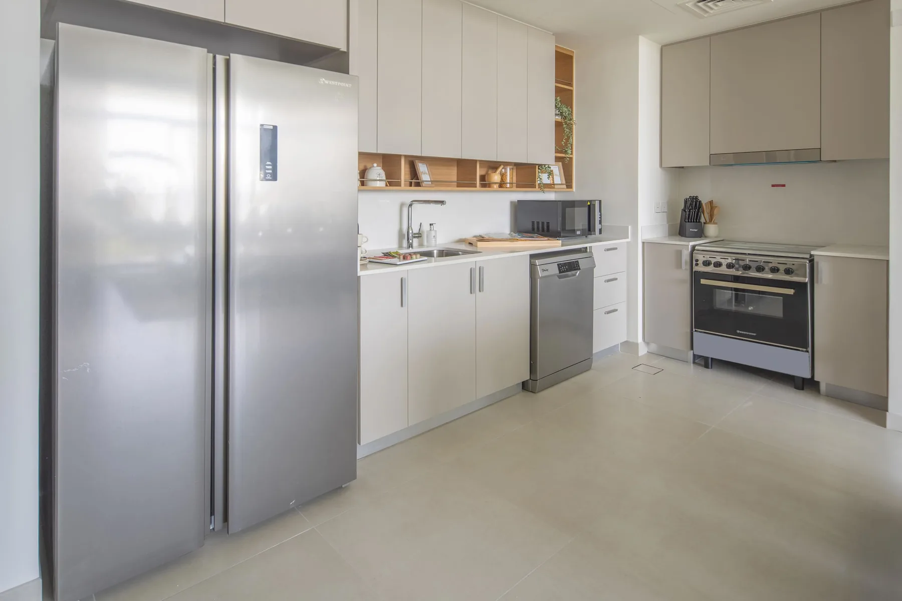 A modern kitchen with pale cabinetry, a large refrigerator, and a cooking range.