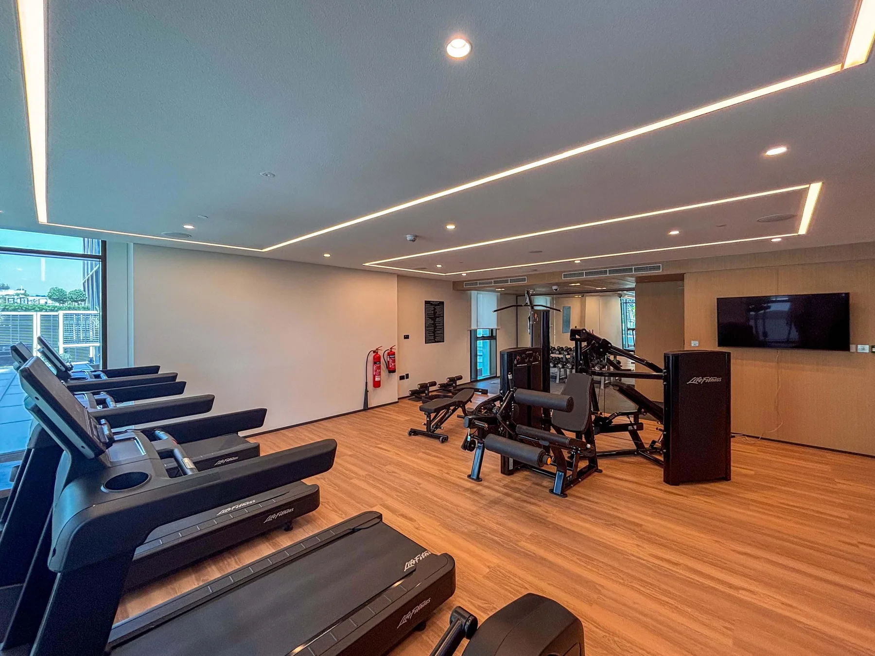 A gym with treadmills, strength-training equipment, and a wall-mounted television.