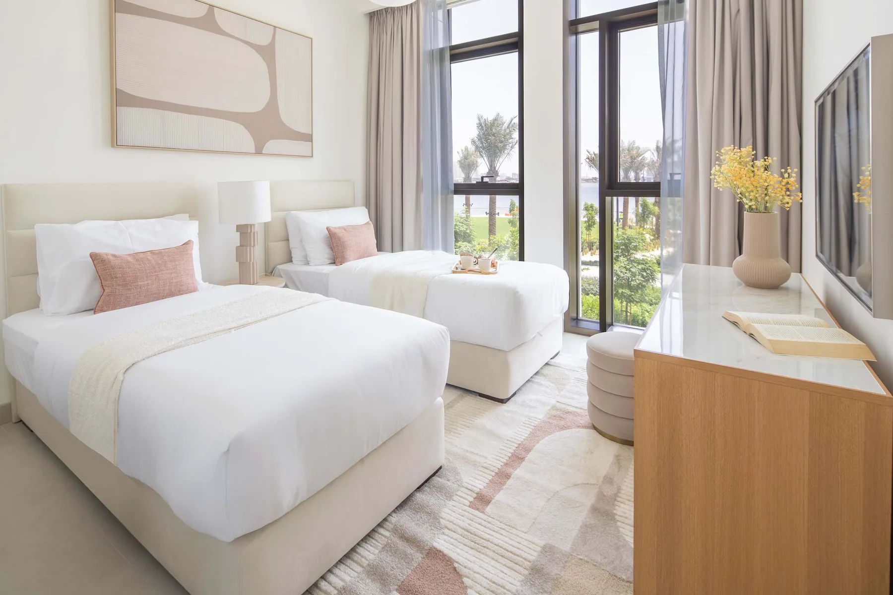 A bright bedroom with two beds, tall windows, and a television.