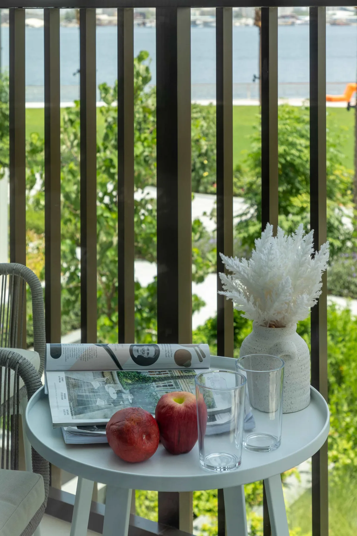 A small balcony table with fruit and glasses overlooks greenery and water.