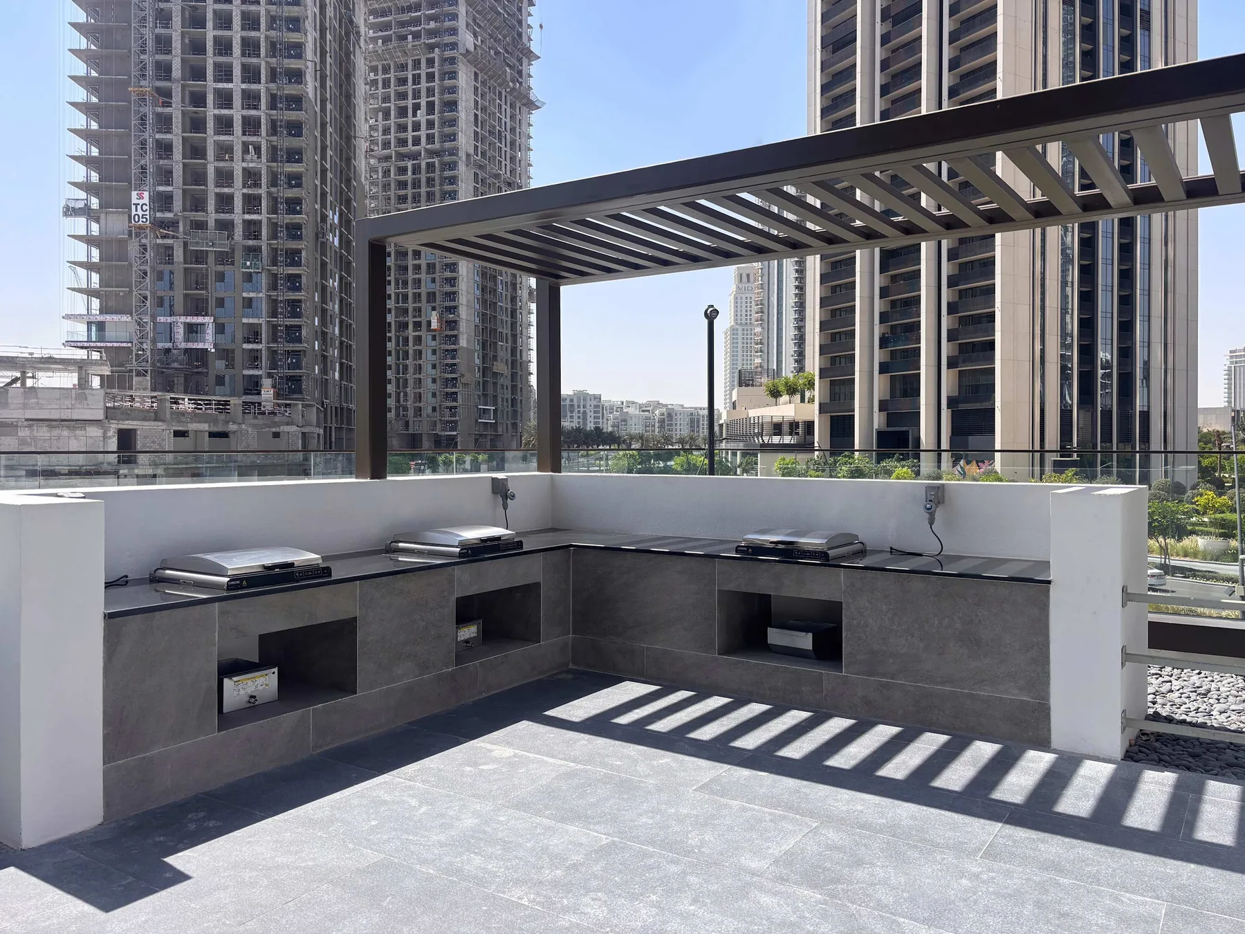An outdoor counter sits beneath a slatted pergola, with high-rise buildings in the background.