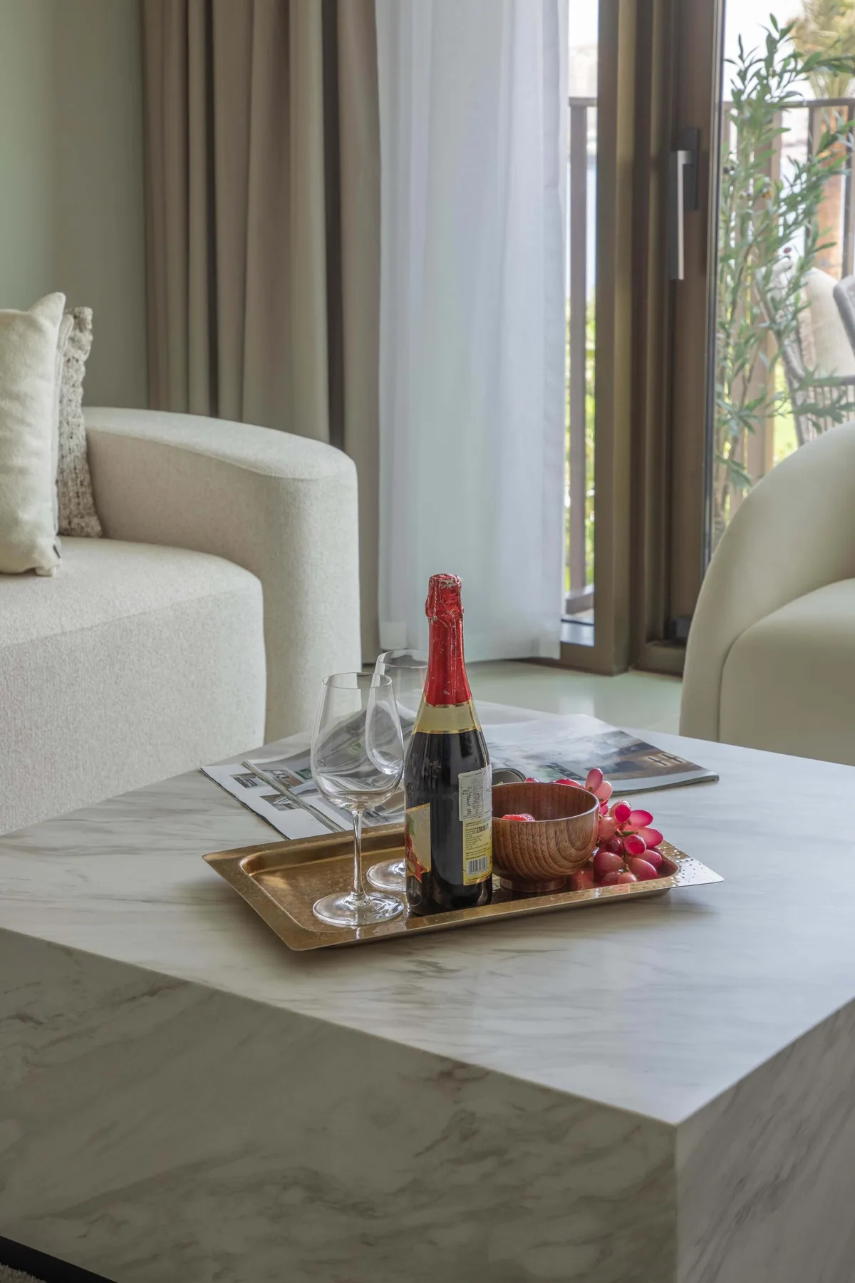 A bright living room with seating around a marble coffee table holding a bottle and glasses.