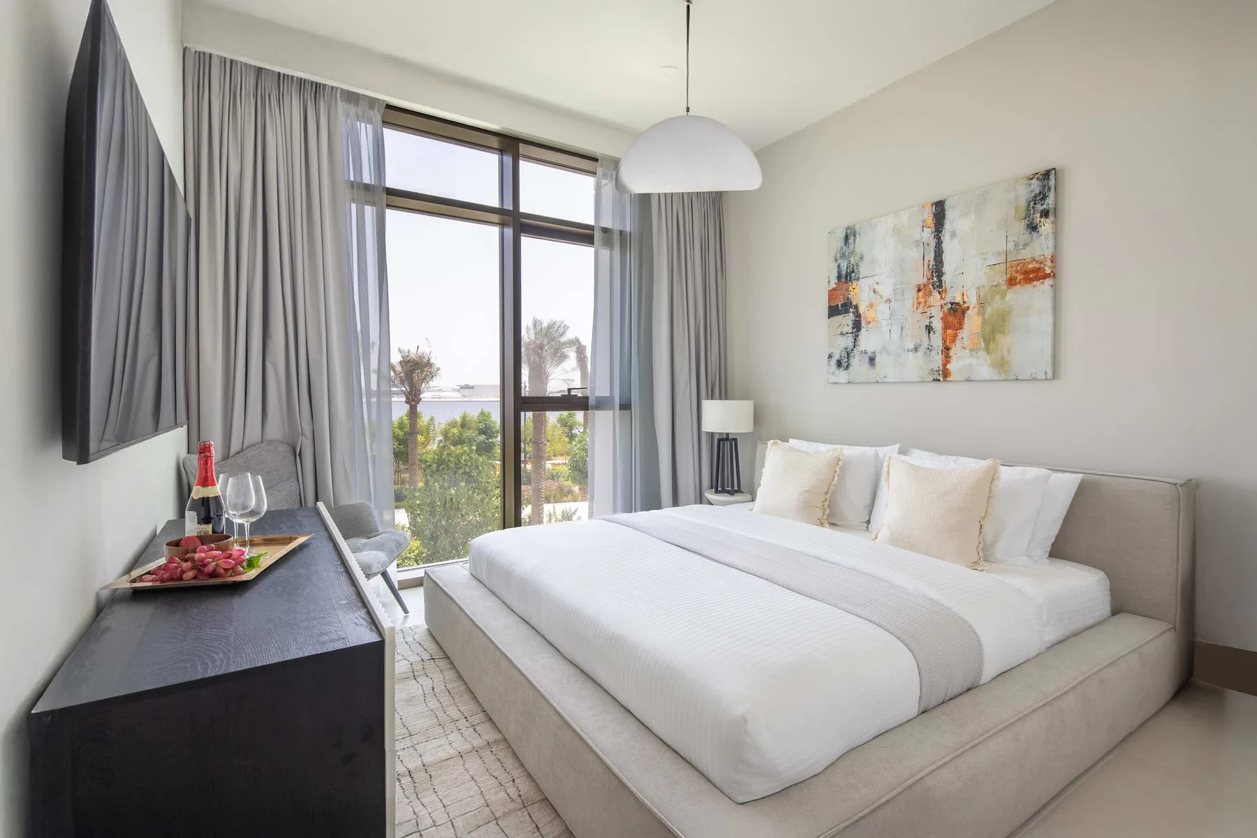 A bright bedroom with a large bed, abstract wall art, and a window.