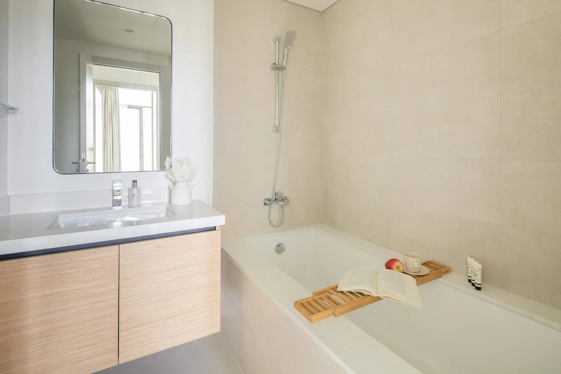 A bright bathroom with a bathtub, shower, and vanity beside a large mirror.