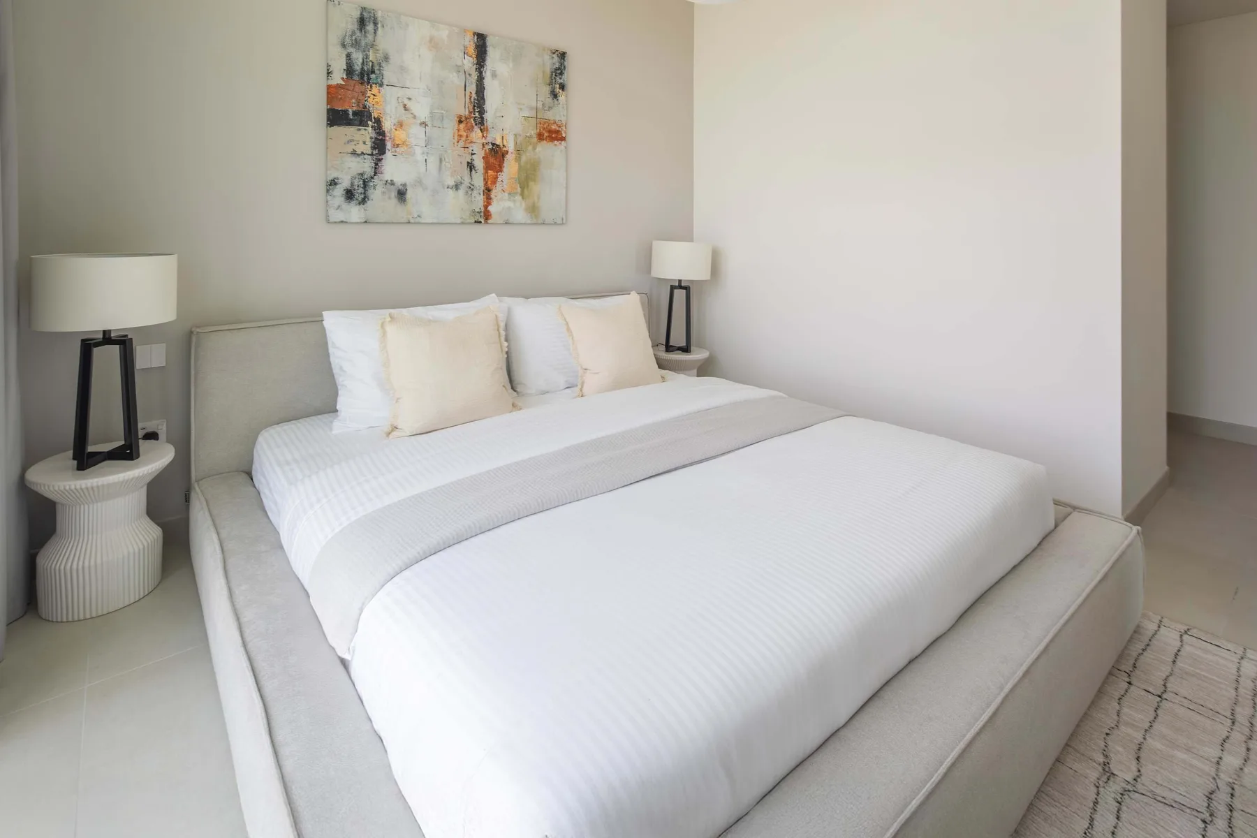 A bright bedroom with a neatly made bed and abstract artwork above it.