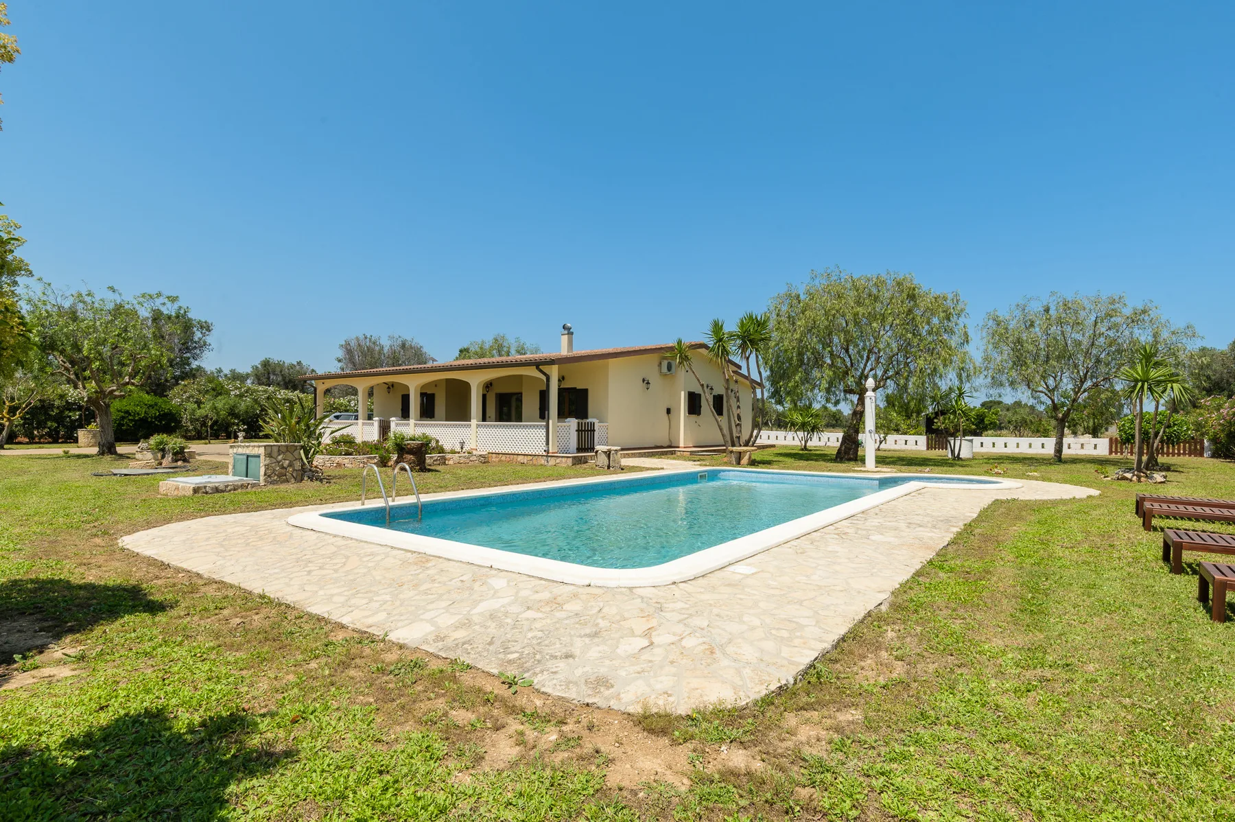 A swimming pool and paved patio sit in front of a single-story house.