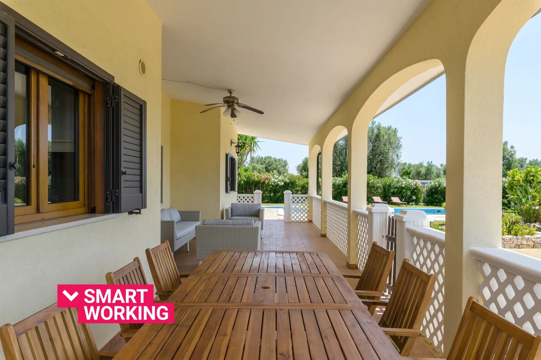 A covered outdoor dining area with wooden tables and views of a pool and greenery.