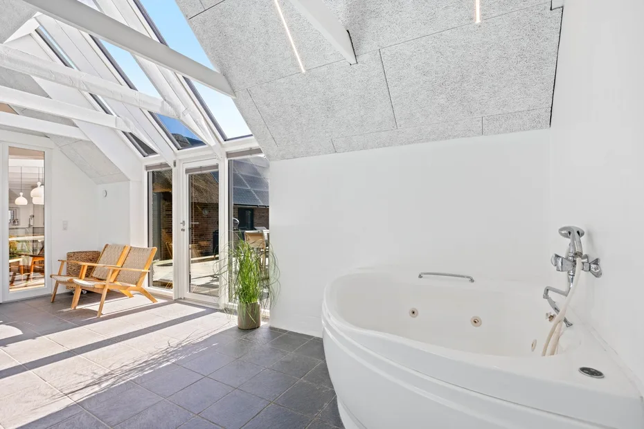 Un baño luminoso con bañera junto a puertas de vidrio que dan a una zona de estar soleada.
