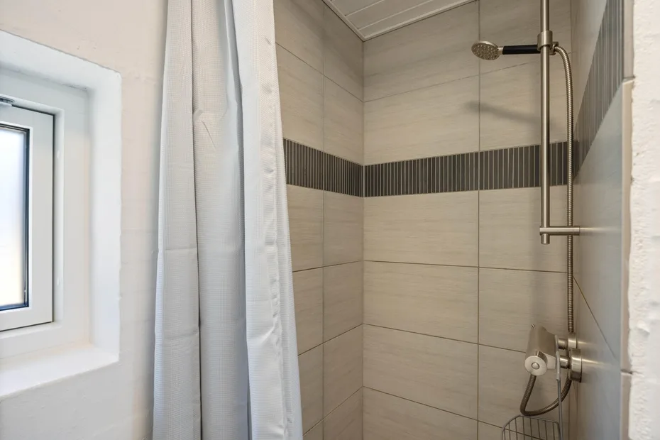 Una zona de ducha con azulejos, una cortina y una ventana pequeña.