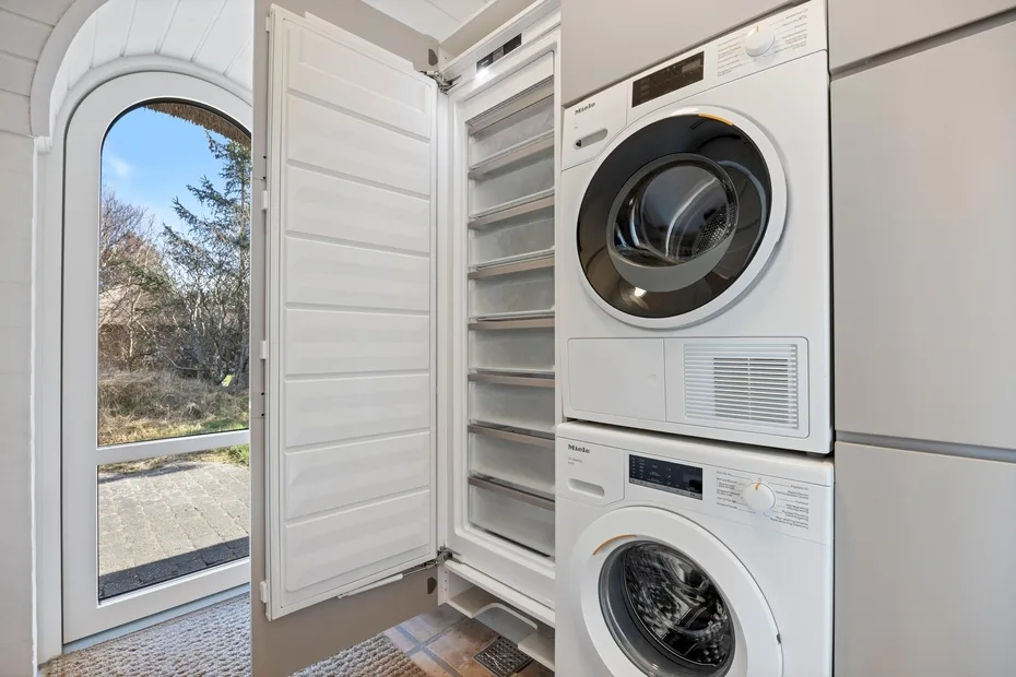 Zona de lavandería con lavadora y secadora apiladas junto a una ventana.