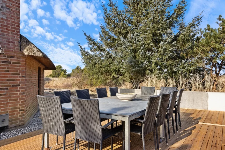 Una zona de comedor al aire libre con una mesa larga y asientos tejidos sobre una terraza de madera.