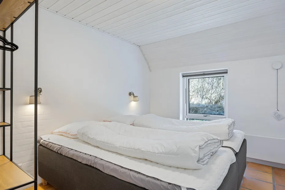 Un dormitorio con una cama bajo un techo inclinado y una ventana.