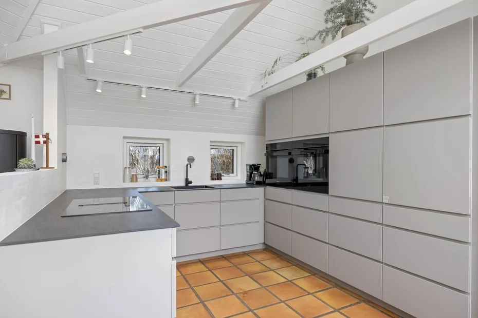 Una cocina luminosa con gabinetes grises, encimeras oscuras y piso de baldosas.